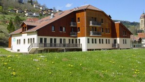 A multi-story building with balconies, set in a grassy area with a hill in the background. - Espace Morteau (Morteau)