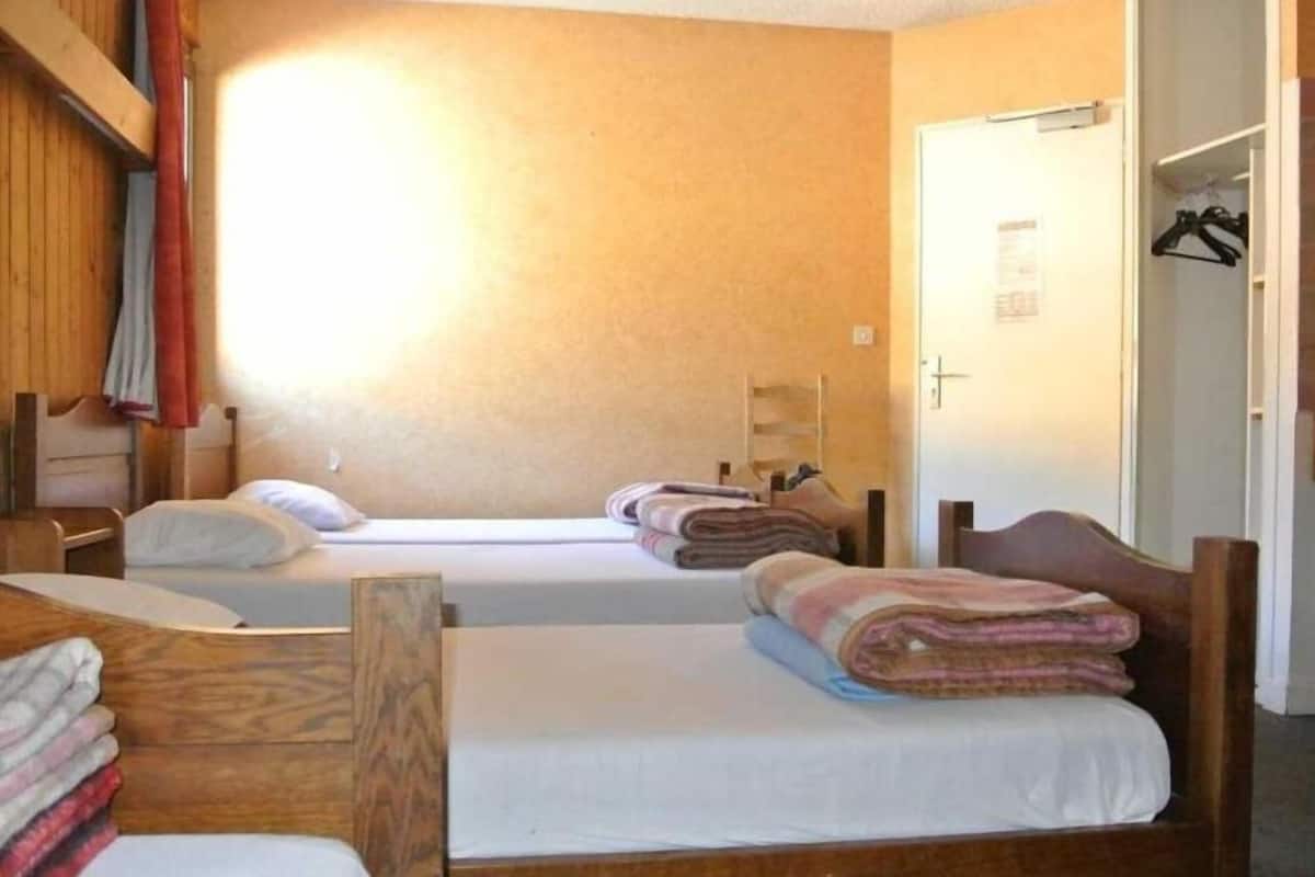 A room with two single beds, wooden headboards, a wooden wardrobe, and a door with a towel rack.