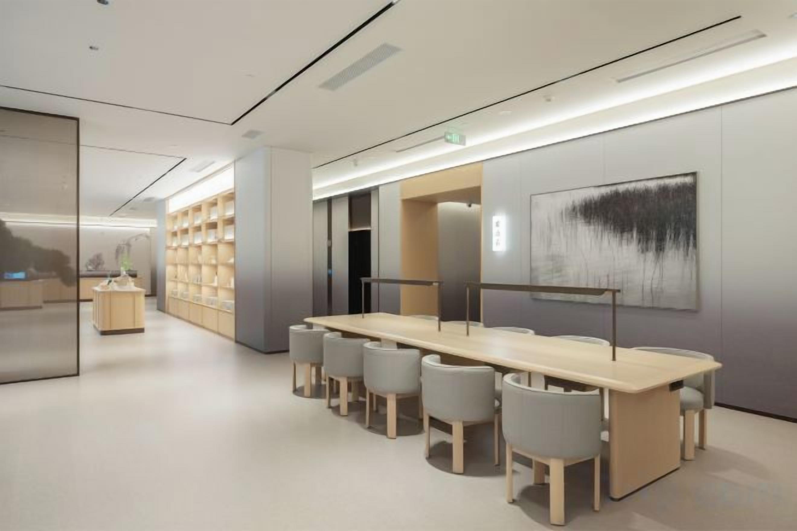A modern interior with a long table and chairs, a bookshelf, and a painting on the wall.