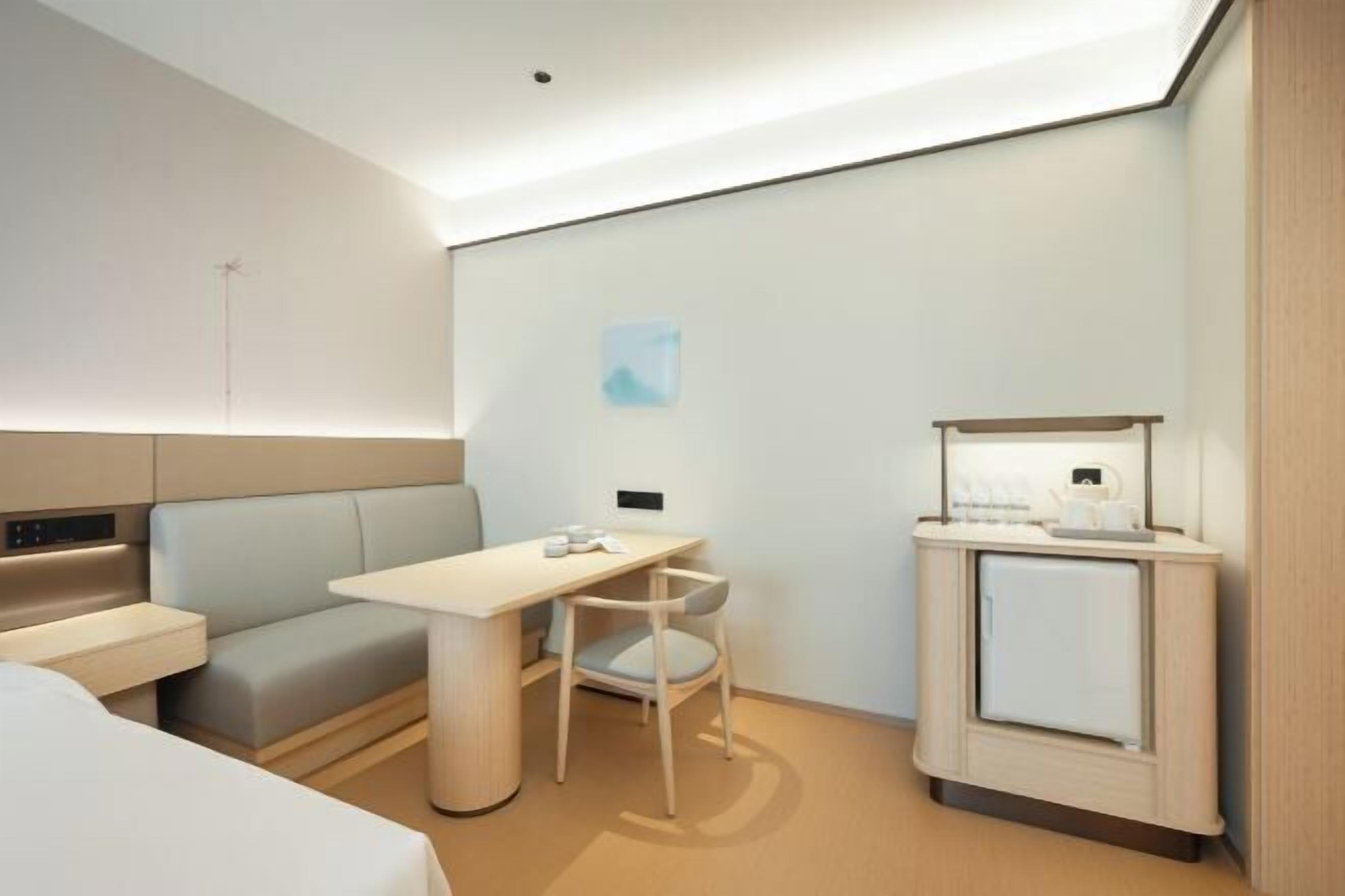 Una camera d'albergo moderna con un letto, una scrivania, una sedia, un piccolo armadietto e un lampadario a parete.