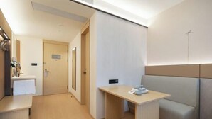 A modern hotel room with a wooden desk, a bench, a small table with a cup, and a door leading to another room. - JI Hotel (Yuncheng Yanhu Tiaoshan Street) (Yuncheng)