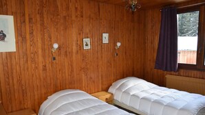 A room with wooden walls, two beds with white bedding, a wooden nightstand, and a window with a curtain. - 3rd floor, balcony, tv, 64m², Pralognan-la-Vanoise (Pralognan-la-Vanoise)