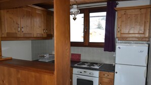 A kitchen with wooden cabinets, a stove, a refrigerator, and a window with a view of the outside. - 3rd floor, balcony, tv, 64m², Pralognan-la-Vanoise (Pralognan-la-Vanoise)