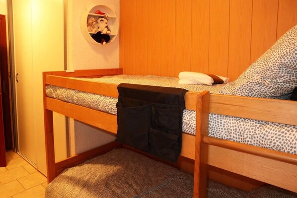 A bunk bed with a storage shelf above it, a small circular window, and a patterned rug on the floor.