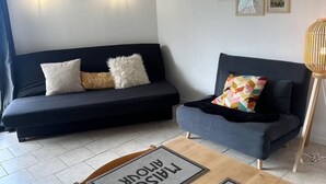 Moderni olohuone, jossa on musta sohva, sininen nojatuoli ja puinen sohvapöytä, jonka päällä on pieniä mattoja.