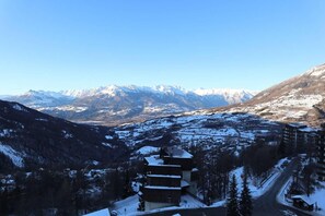 A mountain resort with a view of snow-covered peaks, a ski slope, and a building with a sloped roof.