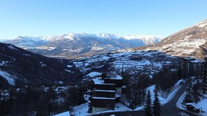 Vuoristomajoitus, josta avautuu näkymä lumihuippuisiin vuorille, jossa on hiihtorinne ja useita kerroksia sisältävä rakennus.