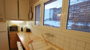A kitchen with a microwave, toaster, and a drying rack. There is a window with a view of a building and snow outside. - 150m from ski slopes, 5th floor, view lake, balcony, tv, ski locker, 50m², Tignes (Tignes)