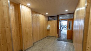 Un corridoio con pareti in legno e pavimento piastrellato, che conduce a un ingresso con porte in vetro.