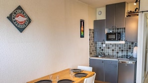 Un angolo cottura compatto con forno a microonde, lavandino e piccolo frigorifero. Si nota un tavolo con quattro sedie e un piccolo oggetto decorativo appeso al muro.