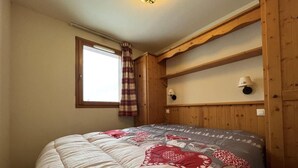 A bedroom with a large bed, wooden paneling, a window with curtains, and a wall-mounted lamp. - 150m from ski slopes, Ground floor, fitness, swimming pool, balcony, tv, ski locker, 38m², Val Cenis (Lanslebourg-Mont-Cenis)