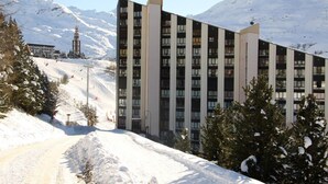Un moderno edificio de hotel con varios pisos y una pista de esquí al fondo.