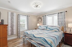 A bedroom with a bed, a nightstand, a dresser, and a window with curtains.