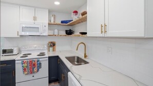 Una cocina con armarios blancos, microondas, estufa, pileta con grifo dorado y repisa de madera sobre la encimera.