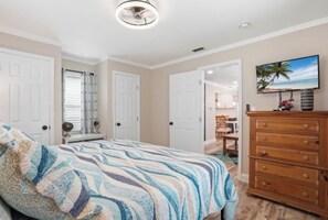 A bedroom with a bed, a dresser, a ceiling fan, and a TV on the wall.
