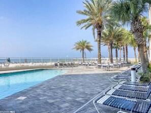 A poolside area with lounge chairs, palm trees, and a view of the ocean.