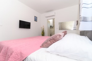 Ett hotellrum med en säng, en platt-TV, en luftkonditioneringsanläggning och en spegel på väggen.