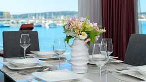 A dining table set for two with a vase of flowers, a view of the marina, and a red curtain in the background. - Luxury 90 m2 Apt.w.balcony & Spectacular sea View (Seget)