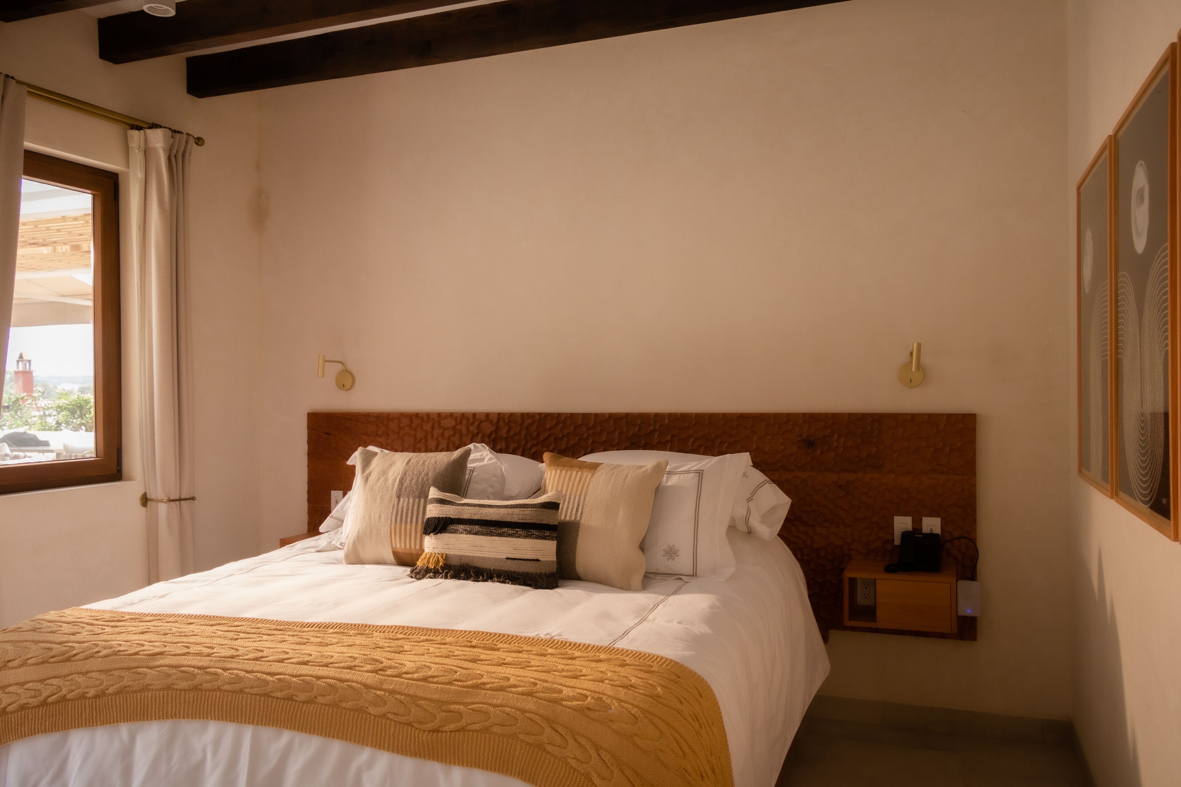 Una cama bien hecha con cabecera de madera, una mesita de noche con lámpara y un cuadro enmarcado en la pared.