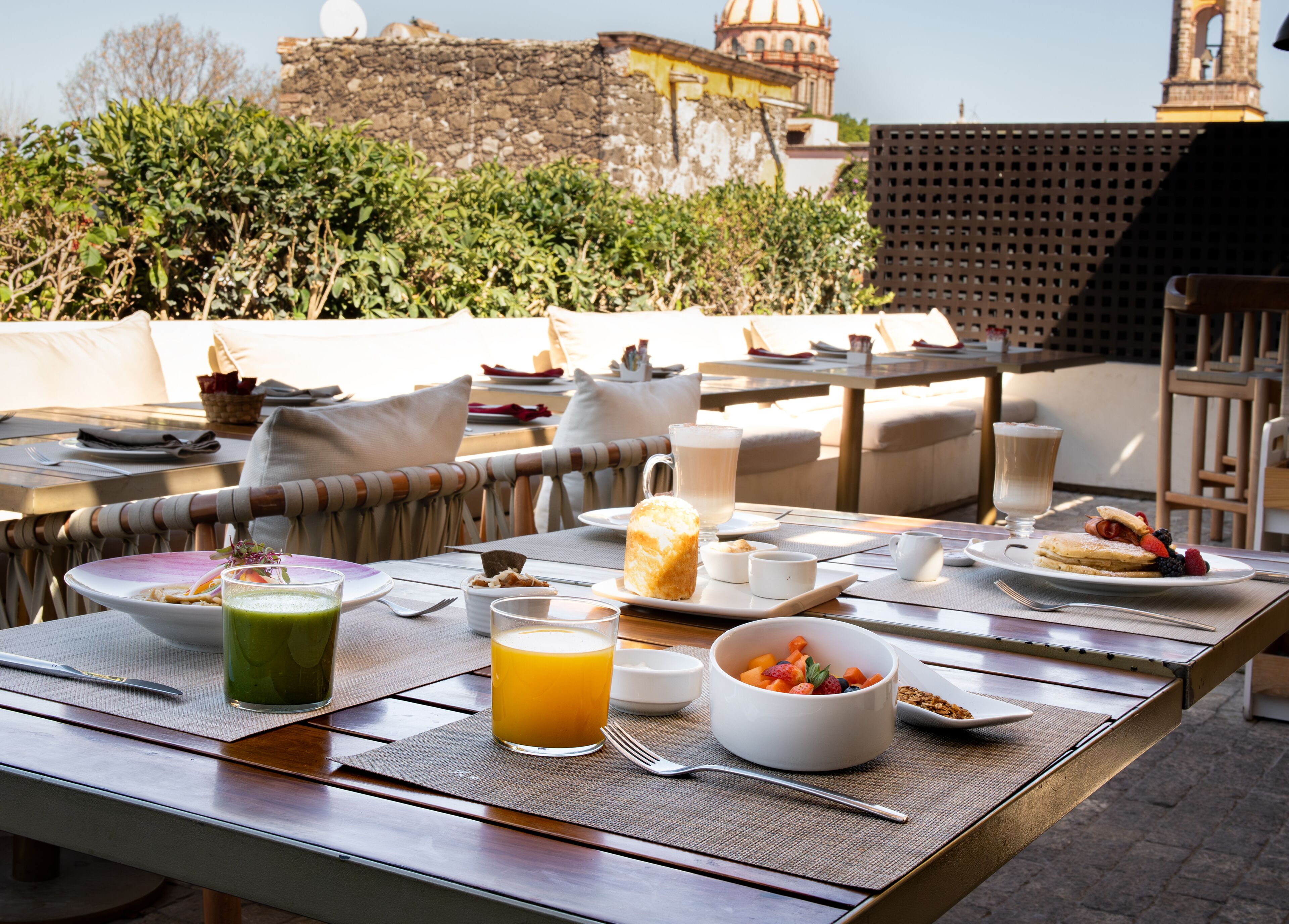 An outdoor dining area with a table set for breakfast, including plates, bowls, and glasses of juice.