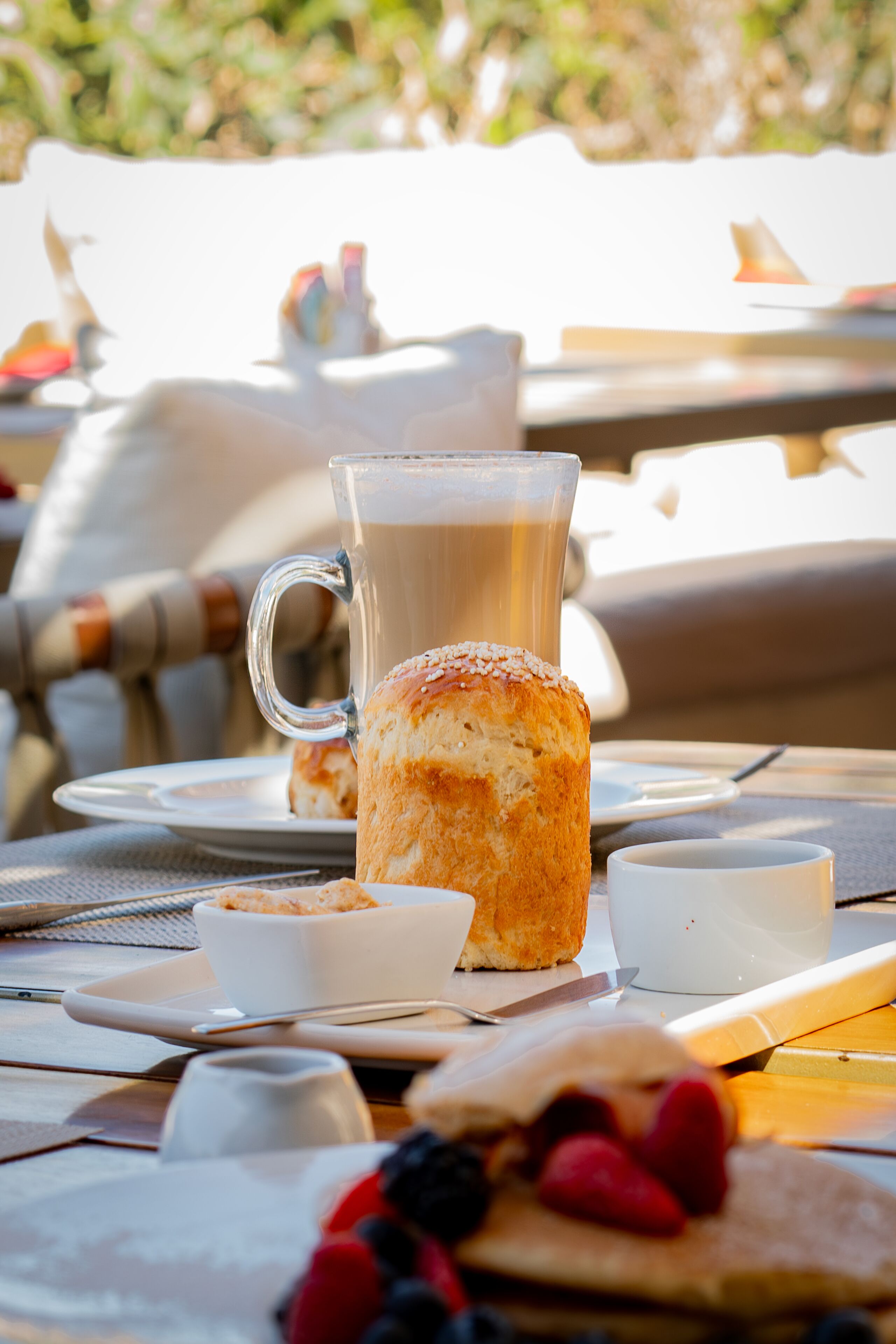 Un desayuno con una taza de vidrio, un bizcocho y frutos rojos sobre una mesa.
