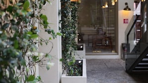 Un patio interior con suelo de ladrillo, una escalera y una pared cubierta de plantas trepadoras.