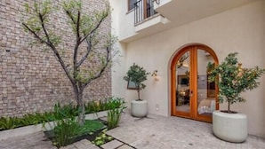 Un patio con pared de ladrillo, plantas en macetas y una puerta de madera.