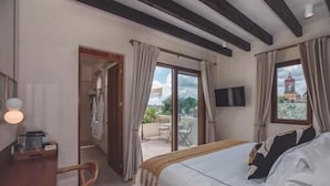 Un dormitorio con cama, escritorio, silla, televisor y balcón con vista a un edificio.