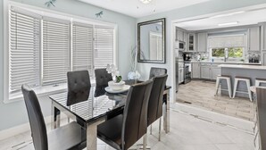A modern kitchen with white cabinets, a central island, and a dining area with a glass table and chairs.