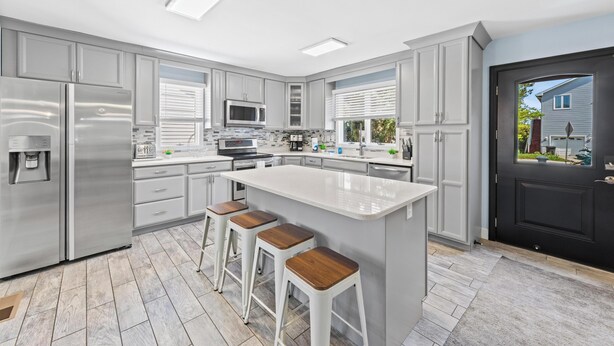 A modern kitchen with stainless steel appliances, a large island with bar stools, and a black door with a view of the outside.