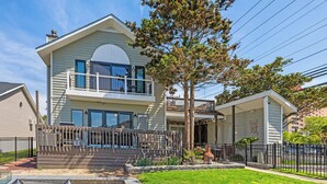 A two-story house with a balcony, a fenced yard, and a tree.