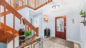 A modern interior with a wooden staircase, a glass railing, a red door, and a small side table with a plant.