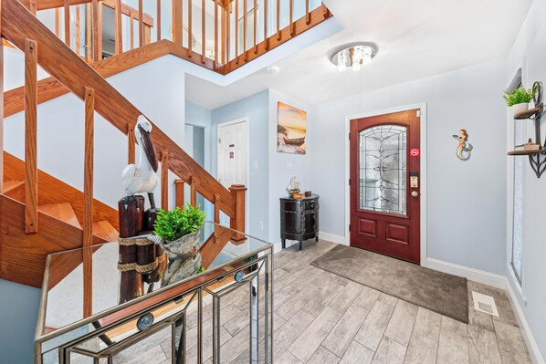 A modern interior with a wooden staircase, a glass railing, a red door, and a small side table with a plant.