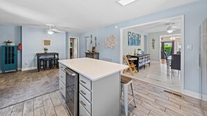 A spacious kitchen with a central island, a dining area with a high chair, and a living area with a ceiling fan.