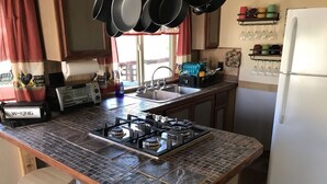 Eine Küche mit Gasherd, Spüle und Kühlschrank. Es gibt Hocker und ein Fenster mit Vorhängen.