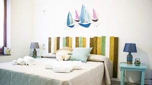 A neatly made bed with pillows and rolled towels, a small table with a lamp, and a wall decoration of sailboats. - Villetta I Pini Azzurri, with large garden and private tennis court (Sardegna)