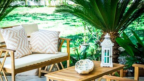 An outdoor seating area with wooden furniture, including a sofa and a table, surrounded by lush greenery. - Villetta I Pini Azzurri, with large garden and private tennis court (Sardegna)