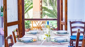 A dining table set for four with plates, glasses, and a bottle of wine. - Villetta I Pini Azzurri, with large garden and private tennis court (Sardegna)