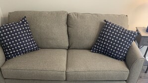 Ein graues Sofa mit gemusterten Kissen und einem Couchtisch mit floralem Mittelstück.