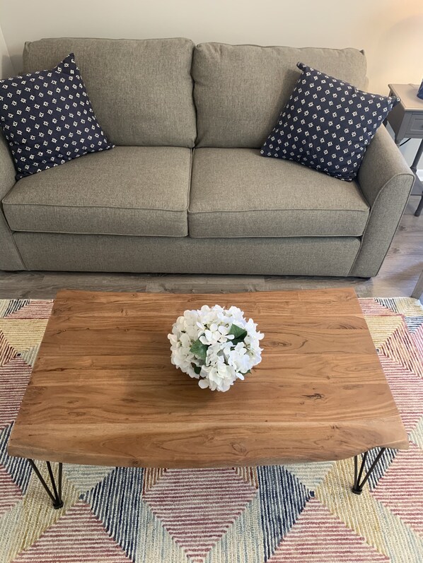 A grey sofa with patterned pillows and a wooden coffee table with a floral centerpiece.