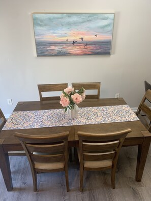 A dining table with a floral table runner, wooden chairs, and a vase with flowers.