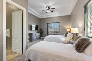 Two beds with white linens and decorative pillows, a ceiling fan, TV, and dresser.