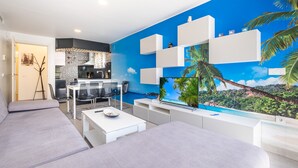 A modern living room with a large TV, a sofa, a dining table, and a kitchen area visible through a glass partition. - Seimar 1-8 Apartment Levante Beach (Benidorm)