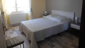 A bedroom with a bed, a nightstand, a lamp, a bench, and a window with curtains.