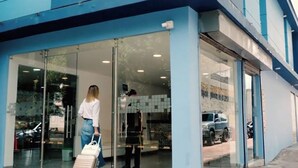 Ein modernes Gebäude mit großen Glasüren, einem sichtbaren Innenraum mit einer Fliesenwand und einem geparkten Auto davor.