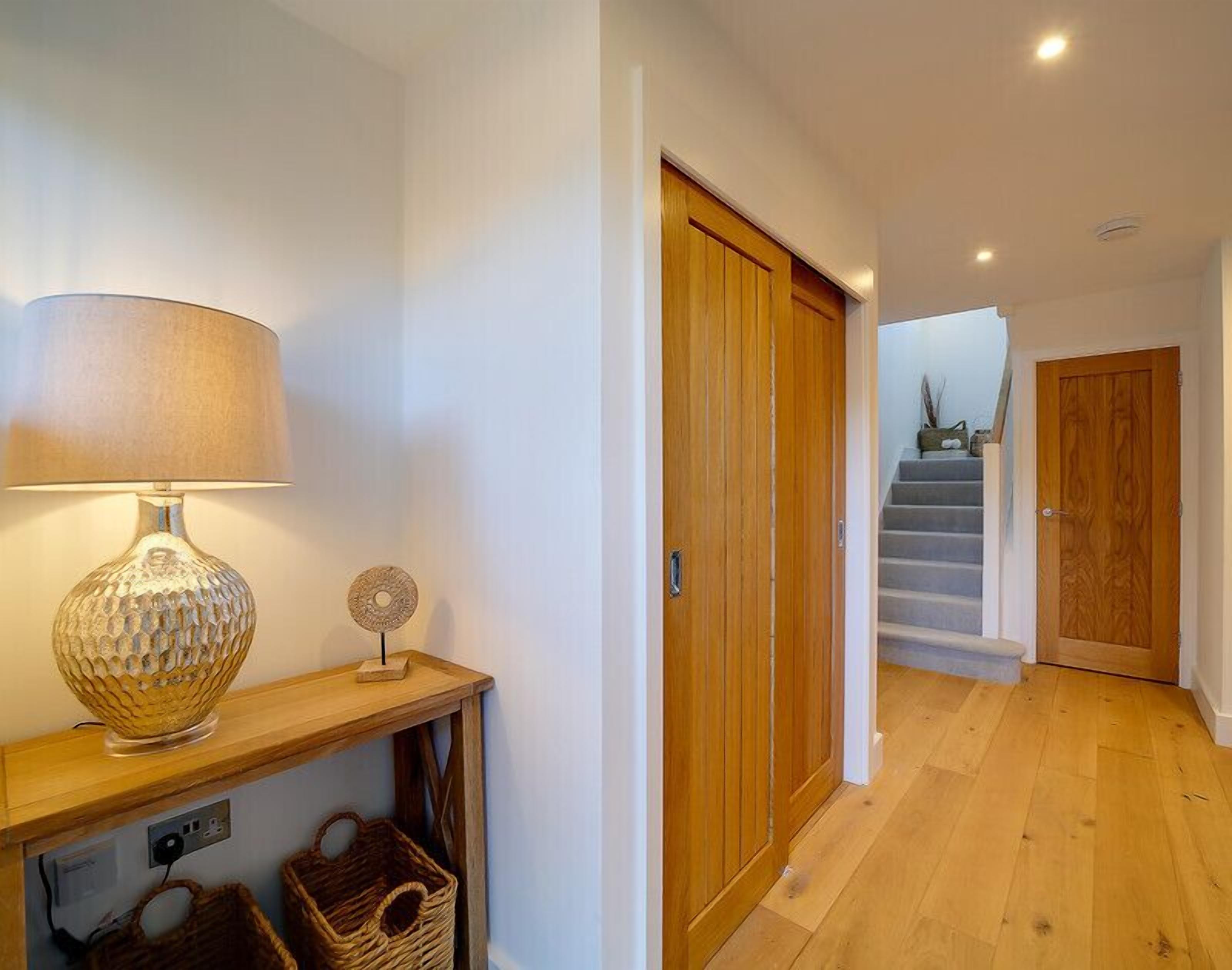 Un couloir doté d’un plancher en bois, d’une lampe posée sur une console et d’une porte donnant sur un escalier.