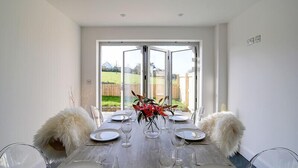 A dining table set for six with clear glass chairs, a wooden table, and a vase of red flowers. - Elmwood (Port Isaac)