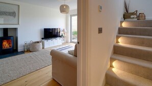 A modern living room with a fireplace, a television, and a staircase. - Elmwood (Port Isaac)