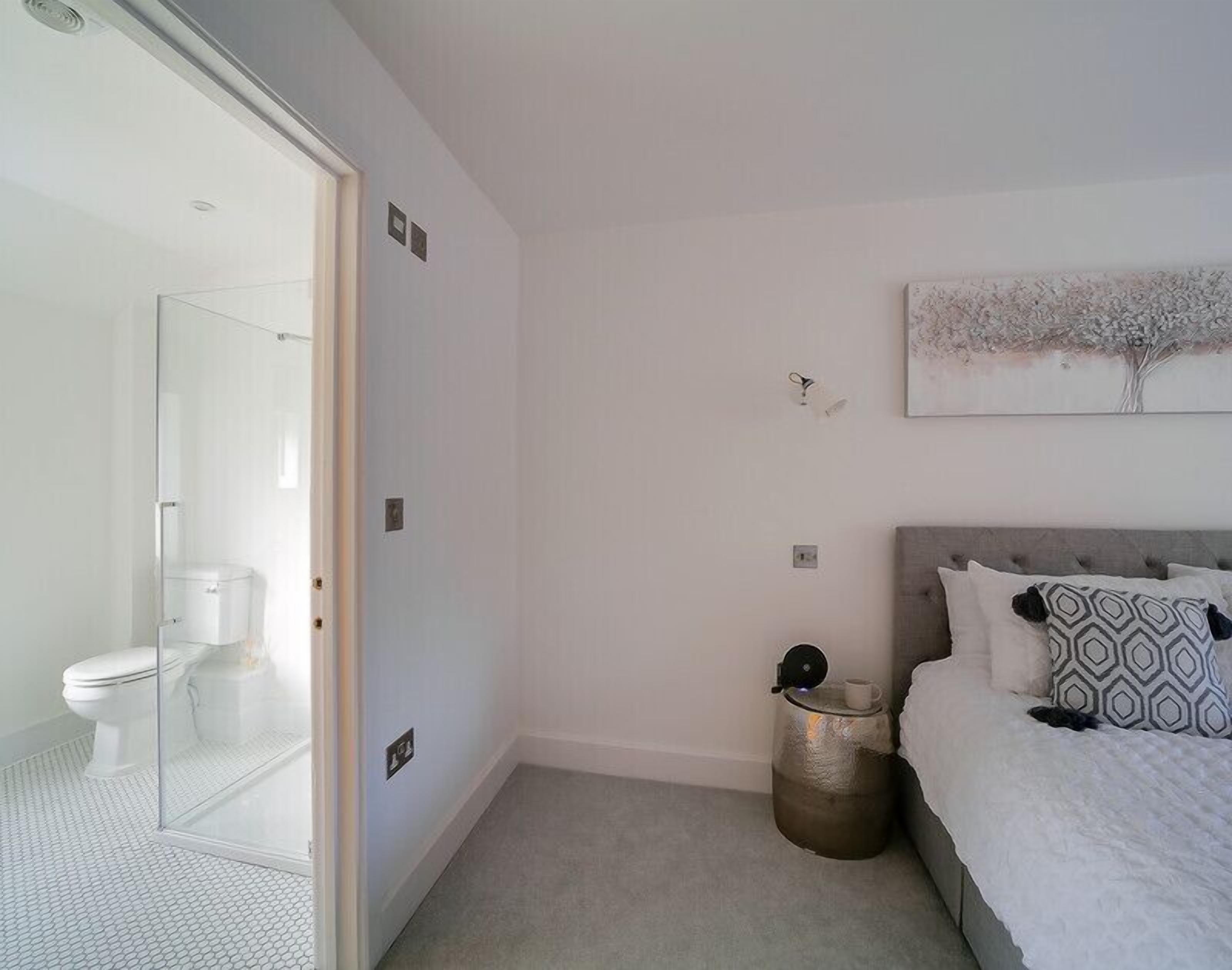 Ein modernes Schlafzimmer mit Duschkabine aus Glas, einem Bett mit gemusterten Kissen und einem Wandbild.