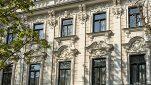 Fachada de edificio con detalles arquitectónicos ornamentales, incluyendo molduras decorativas y marcos de ventanas.